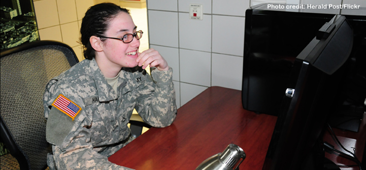 Image of smiling female soldier seated at computer workstation